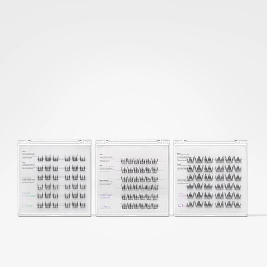 Three clear plastic trays of false eyelashes arranged side by side on a plain white background. The lashes are black and arranged in different patterns: vertical, wavy, and layered.