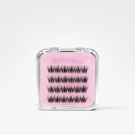 A pair of black false eyelashes in a clear plastic case with a pink insert labeled 'Blush Macaron' on a light gray background.