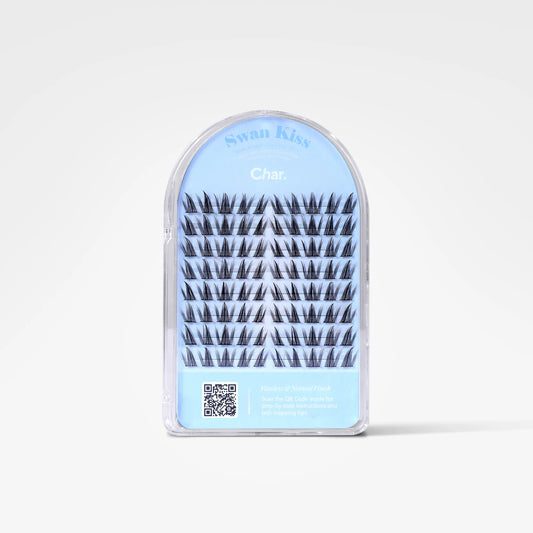 A package of false eyelashes in an arched clear plastic case with a light blue insert. The lashes are black, and the packaging features the brand name 'Swan Kiss' and the shade name 'Char.