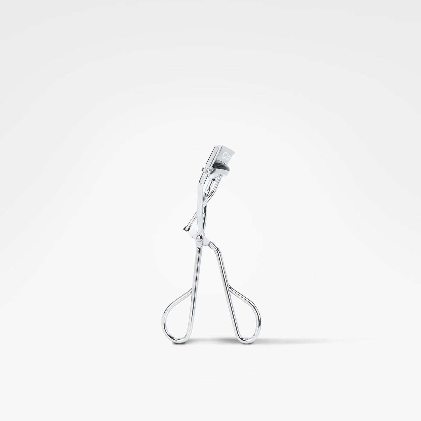 A silver metal eyelash clamp shown from the side against a clean white background.