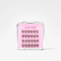 A clear plastic clamshell case containing false eyelash clusters on a pink backing card labeled 'Sugar Puff' and 'Clás', photographed on a clean white background.